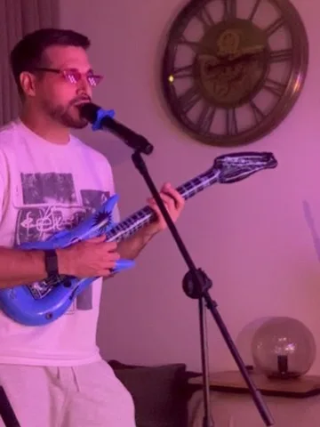 Guest with pink glasses playing an inflatable guitar while singing